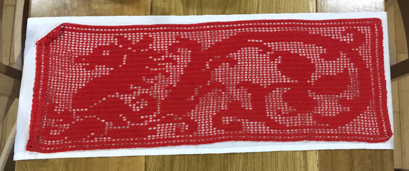 Lacey Crochet table runner showing a red dragon in the crochet equivalent of pixel art. White cloth background.