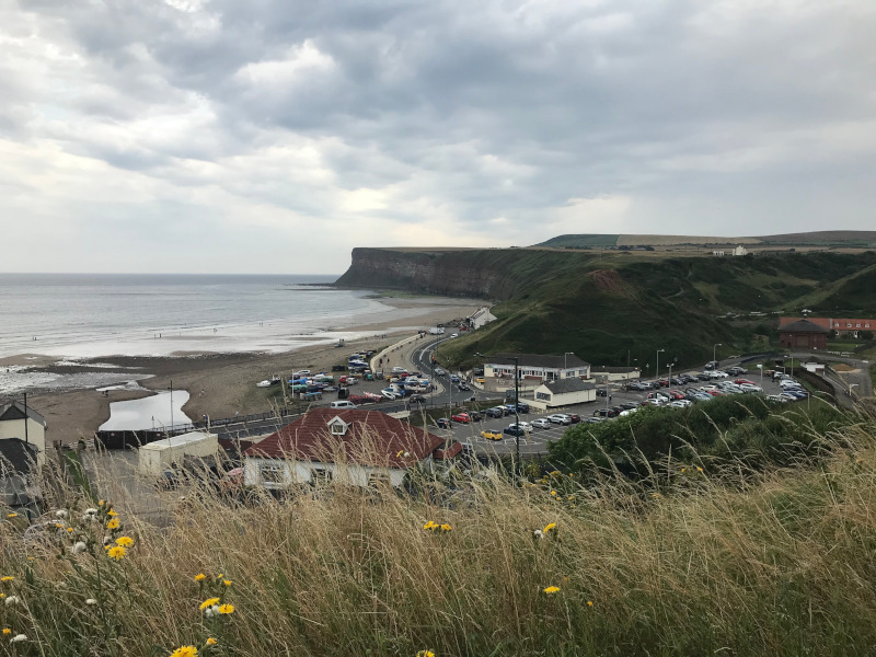 Looking down onto a beach with a pub and cliffs in the background.