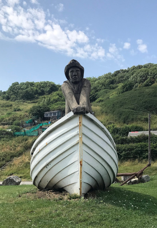 Wooden sculpture of a sailor standing in the prow of an old fishing boat.