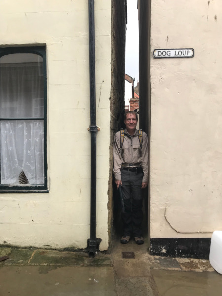 B. squeezed into a tiny gap between two houses with the sign 'Dog Loup' next to it.
