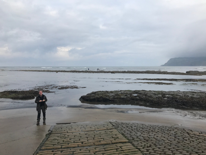 B. standing on a beach at the end of a brick slipway.