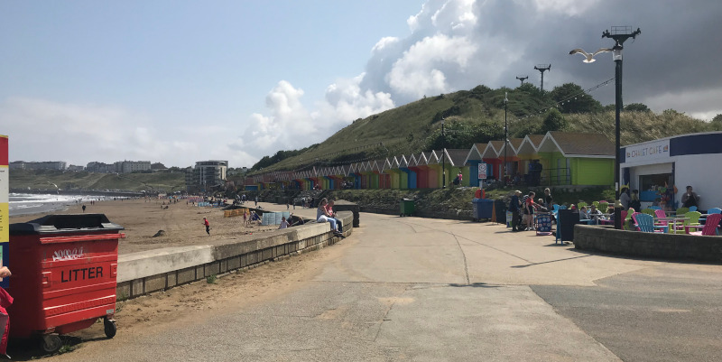 Scarborough Promenade with multi-coloured beach huts on the right and the beach on the left.