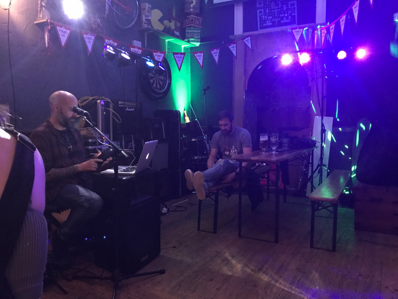 Dark green and purple pub interior. Bald man with a MacBook sits on the left.