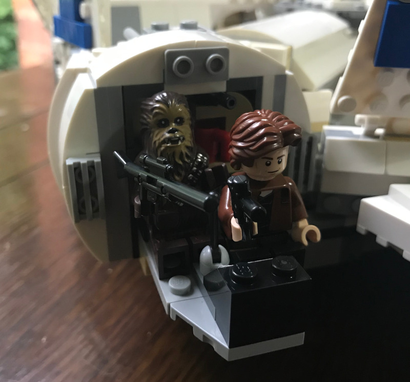The cockpit again. The glass front has been removed to reveal Han Solo and Chewie, both holding guns (in Chewie's case a long rifle), crammed together in the small space inside.