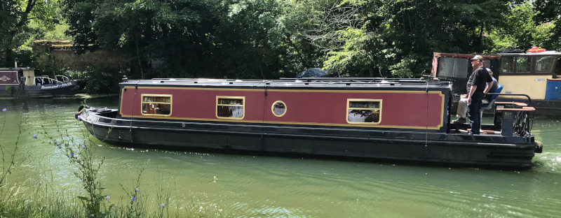 Photo of a red narrow boat on a rather green looking stretch of the Thames.