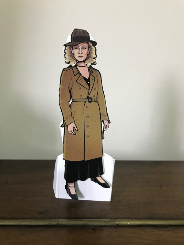 Paper doll of River song in long overcoat and hat.