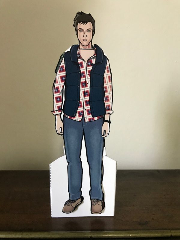 Rory Williams Paper Doll in jeans a checked shirt and a puffy sleeveless jacket.