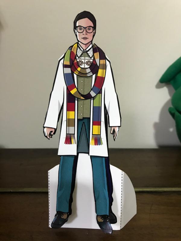 Paper doll of Osgood wearing a white coat and the Fourth Doctor's Scarf.