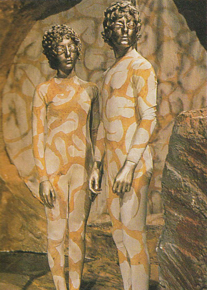 Two Axons in their human like form with golden faces and white and gold jumpsuits.