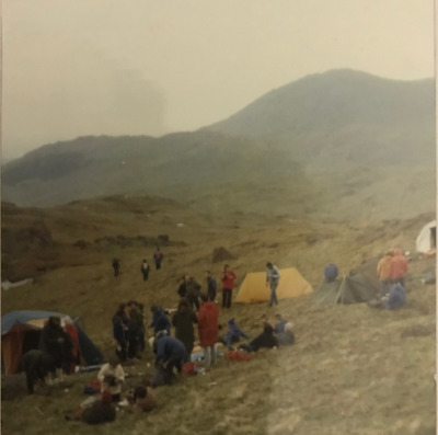 A misty and damp photo of mountains, tents and campers.