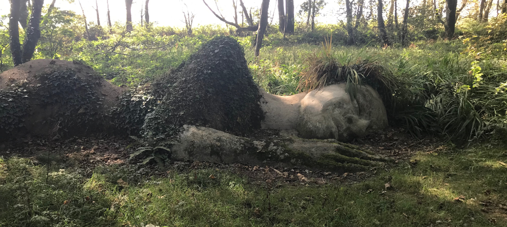 Mud statue of a sleeping woman covered in ivy and lichen with leafy plants as hair.