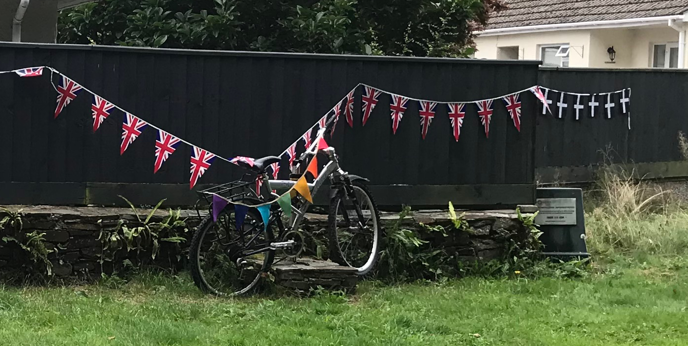 Bicycle against a fence draped in Union Jack and Cornish flag bunting.