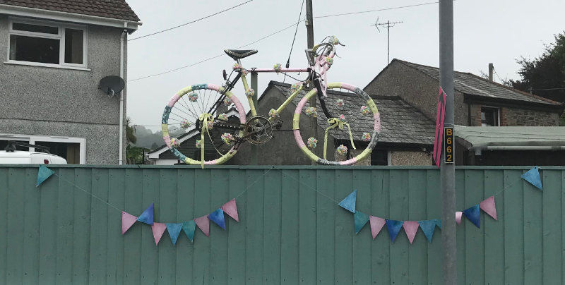 Pink and Yellow decorated bike with flowery pom-poms on a fence with pink and blue bunting