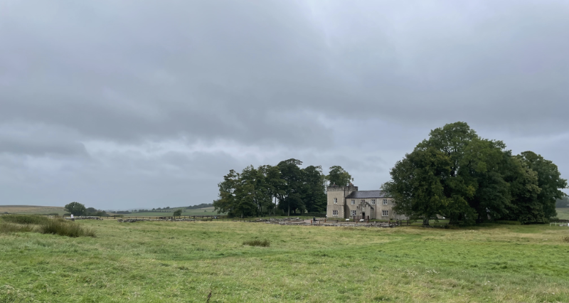 A grand victorian building with square tower amid trees.  Low remains of walls just visible in front of it.