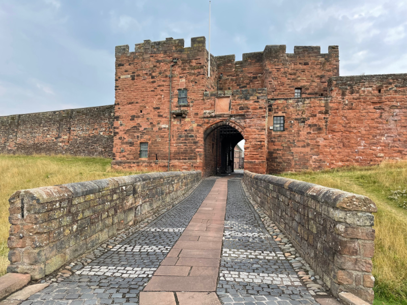 A bridge leading to a red brick gateway with battlements and asymetrically placed windows.