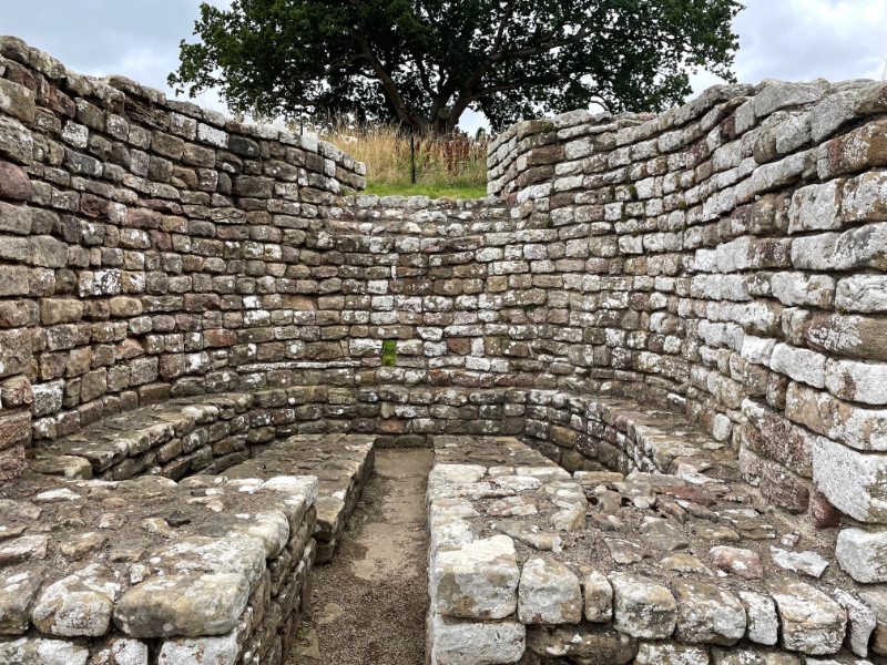 A semi-circular room with high walls and stone benches around the edge.