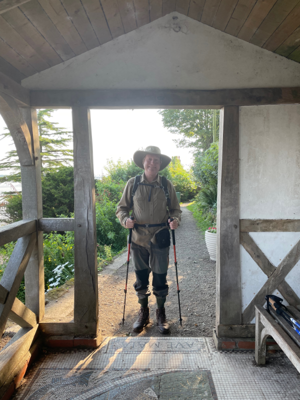 B standing in fake Roman shelter in a wide-brimmed hat with walking sticks.