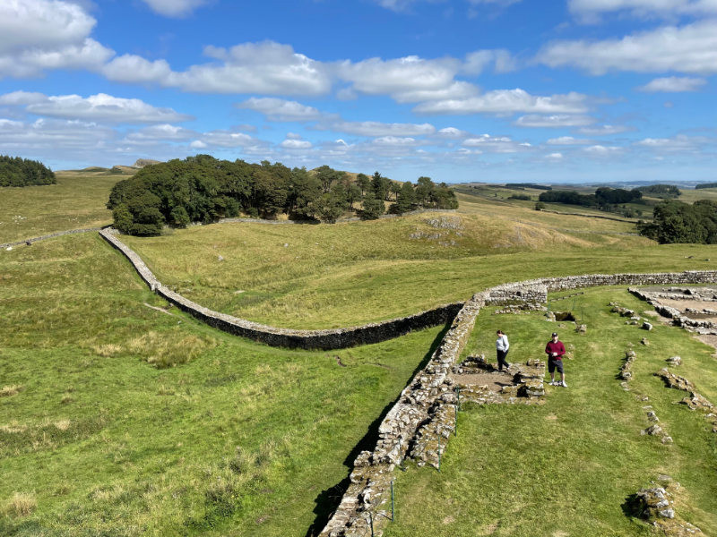 Looking down from above on the wall of the fort and Hadrian's Wall stretching from its corner out across the fields.