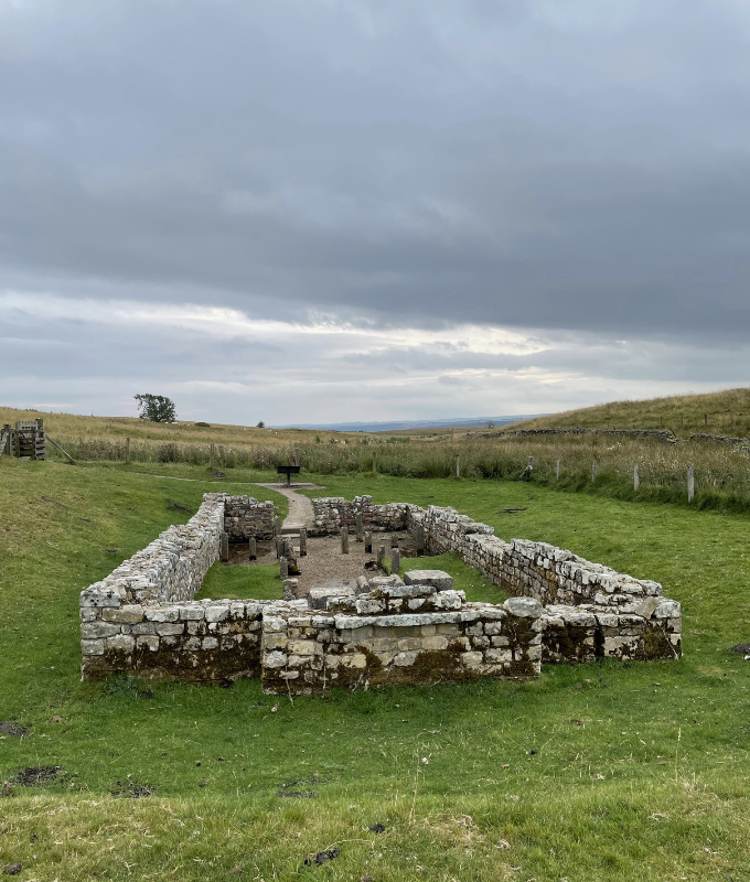 Rectangular low walls.  At the far side a pathway leads in at an entrance.  Small stone markers form an aisle down the centre of the building.