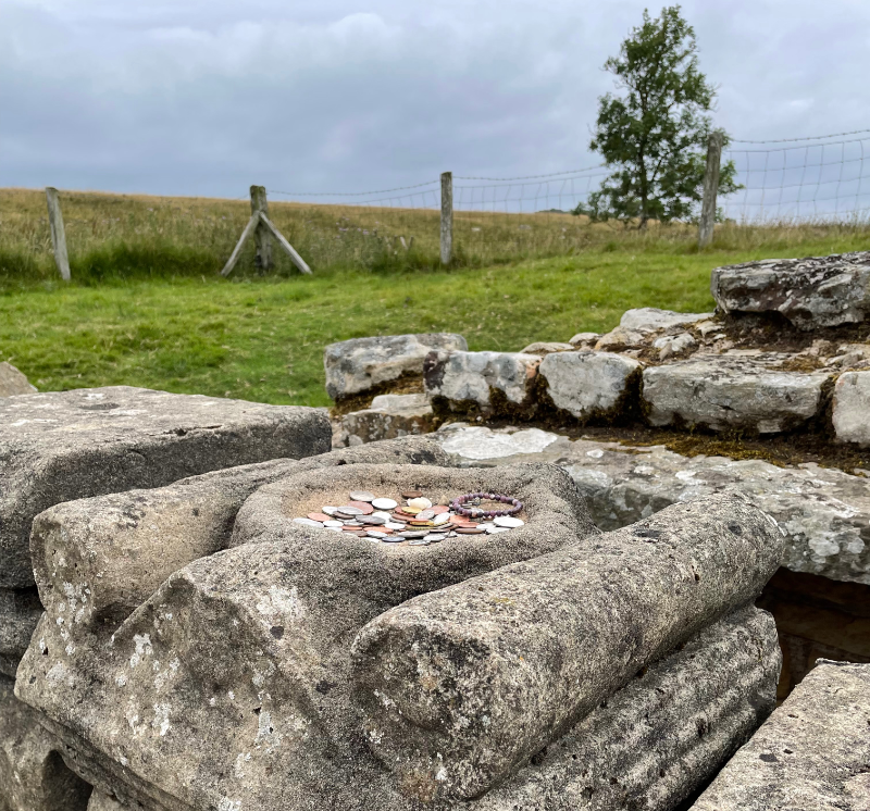 Top of a stone altar with pennies and a small bracelet left in it.