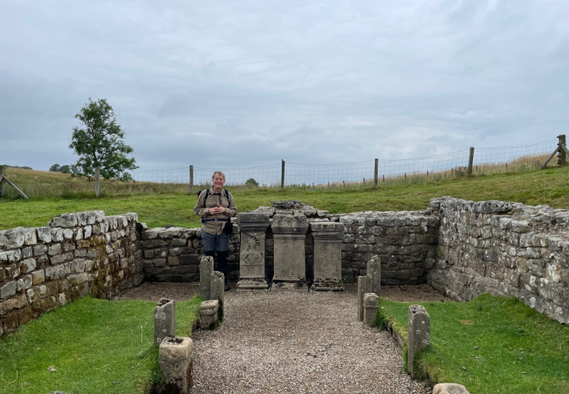B. stands next to three upright stones at the end of the building.
