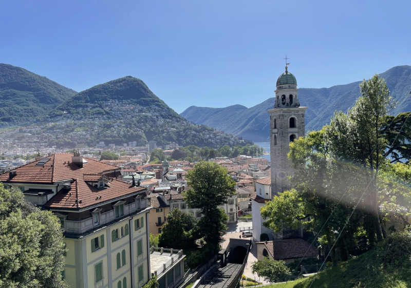 View down to the city with wooded mountains in the background and clock tower to the right.