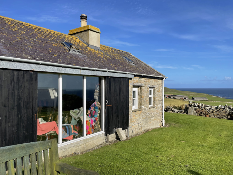 A long low house with a picture window and a clear blue sky beyond.