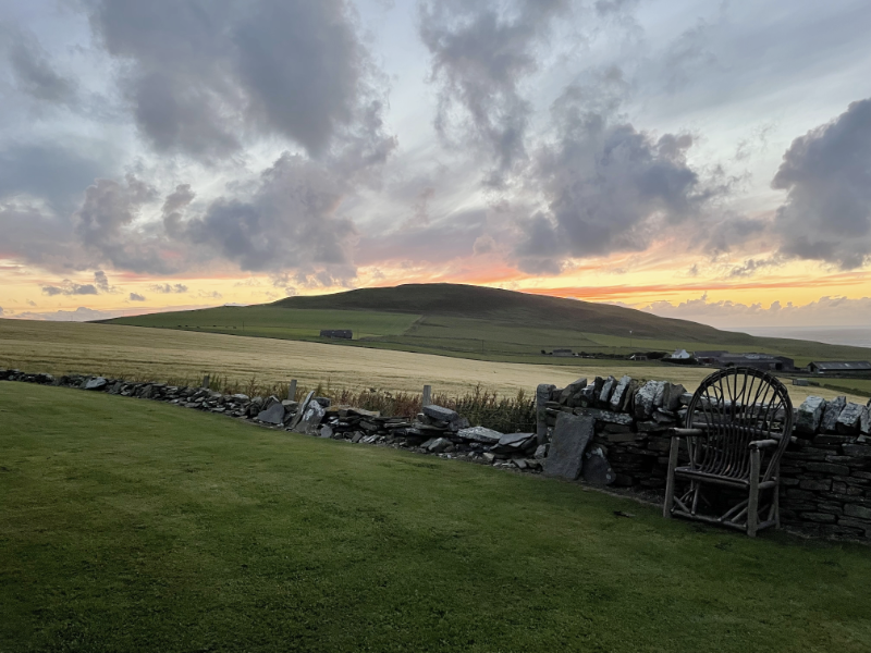 View of the dry stone wall, hill and sunset again, but this time showing a wooden chair against the wall.