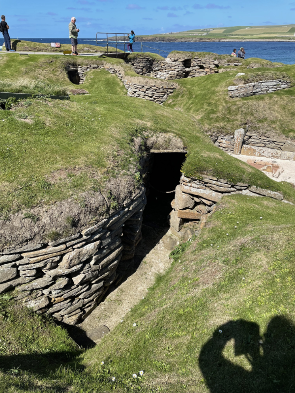 Grass covered sand dunes, revealing a curved wall leading into a dark entrance.