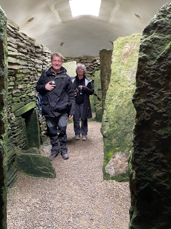 B and Aerin inside a tomb. A false white roof with skylight is overhead. Upright stones divide the walls.