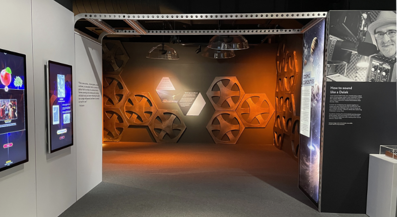 Arch through to wall decorated with cog style roundels from the Thirteenth Doctor's Tardis.  Bonus photo of Nick Briggs to one side.