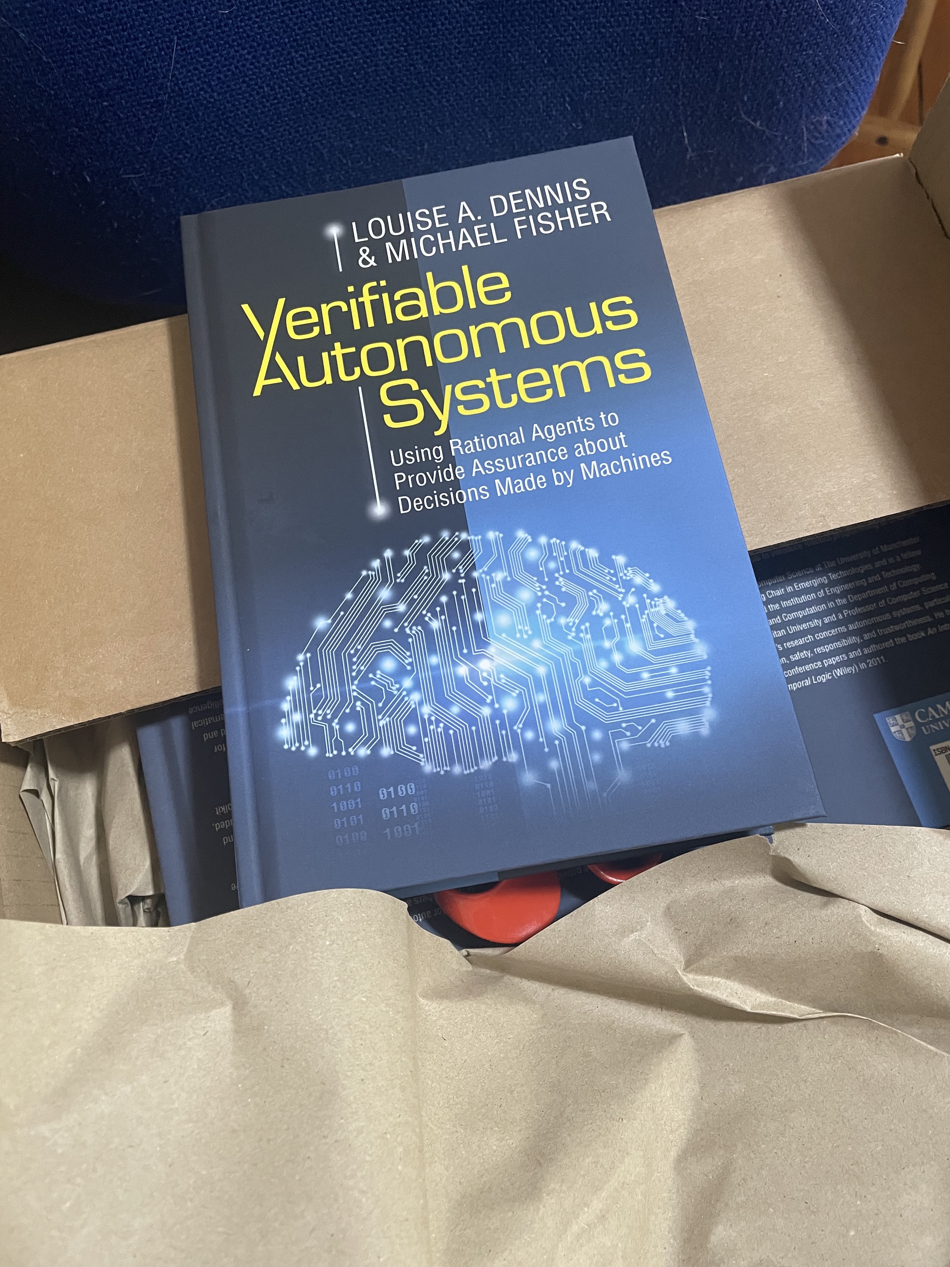 Copy of Verifiable Autonomous Systems by Louise A. Dennis and Michael Fisher on top of a cardboard box.  More copies can just be seen inside the box.