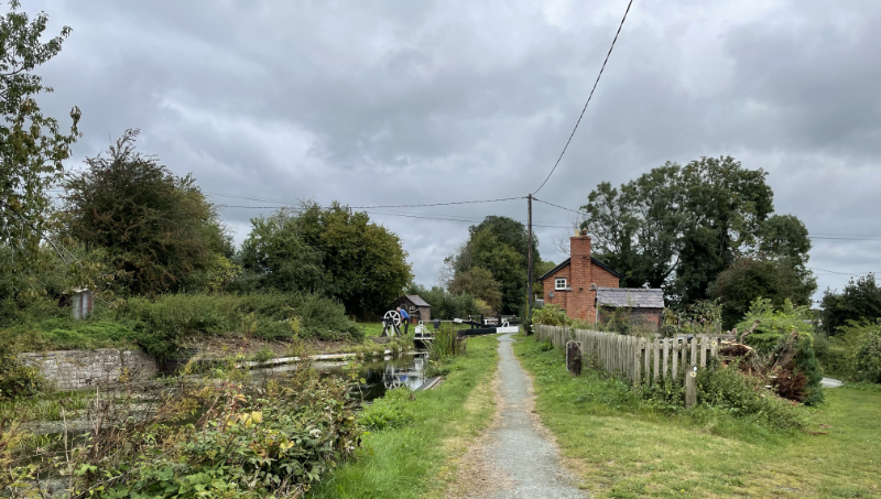 A lock across the canal with a small cottage and a white wheel for operating the lock.