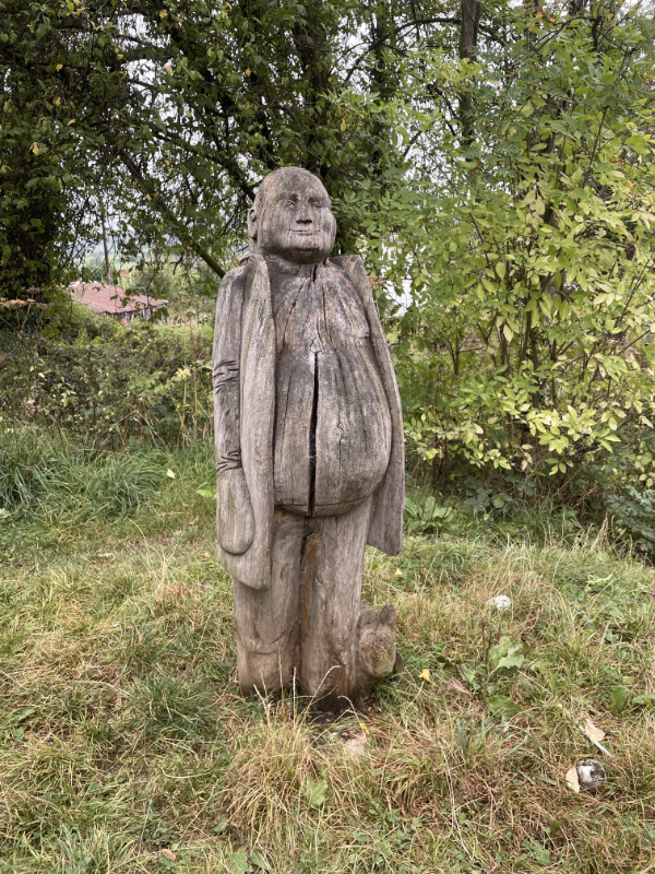 A plump wooden man. Bald with his hands in his pockets.
