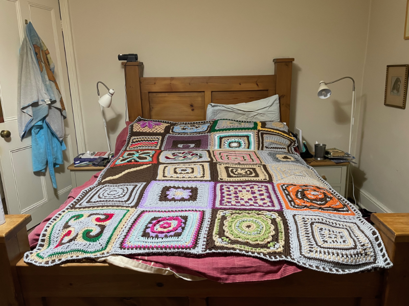 A blanket made from 24 large crocheted squares on a double bed