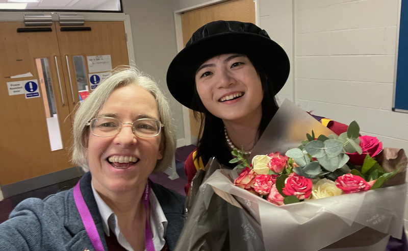 Selfie of me and a Chinese girl who is wearing full academic regalia and holding a bunch of flowers.