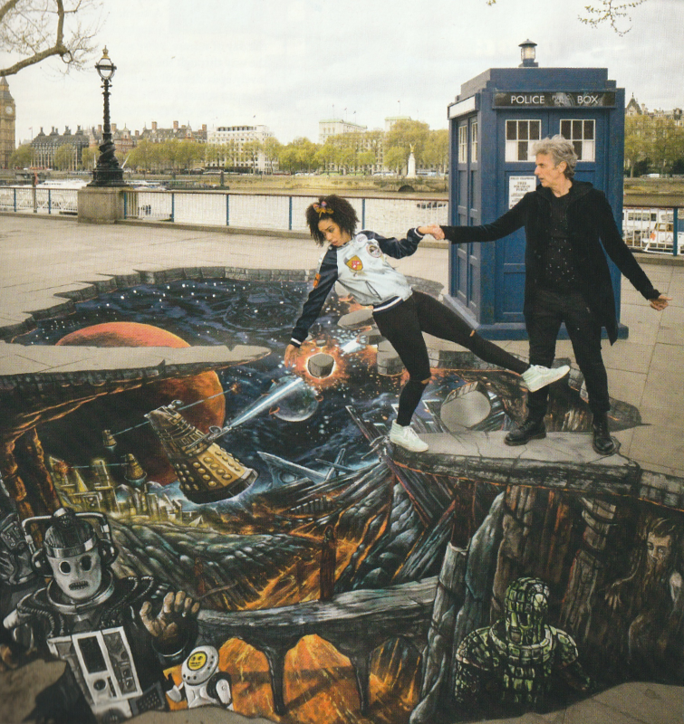 Peter Capaldi dressed as the Twelfth Doctor outside the Tardis on a railed promenade next to a river.  He is holding the hand of Pearl Mackie as Bill.  She is standing on one leg and leaning backwards over a piece of street art on the flags showing a fiery pit that contains Cybemen, Ice Warriors and other creatures.  Daleks flout of the pit against a backdrop of a large planet and stars.  There is a stone bridge over a river of lava.  The art is drawn convincingly to look like the flags have crumbled away to reveal this world below.