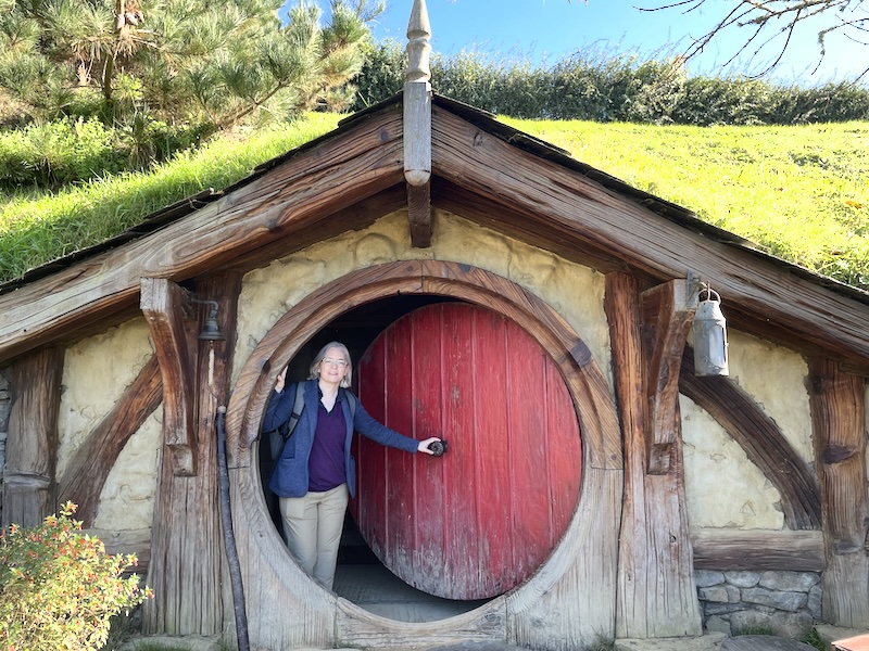 Me standing in the doorway of a hobbit hole with a red door.
