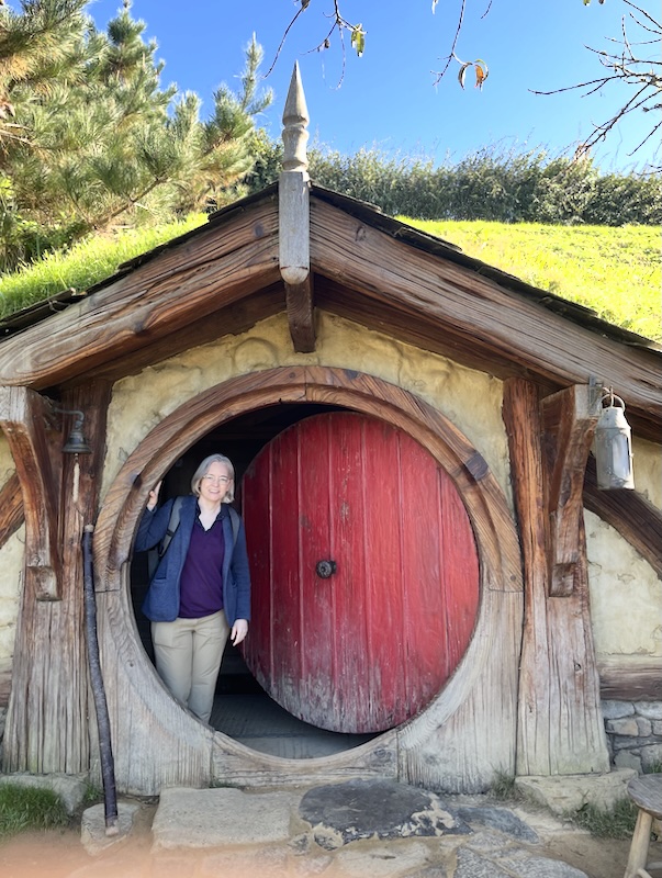 Me standing in the doorway of a hobbit hole with a red door.