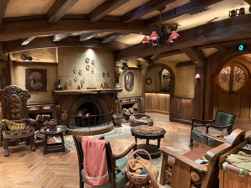 A living room with a curved ceiling with wooden beams. Wooden chairs and tables and a fire place.