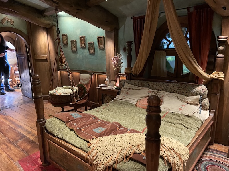 A double bed with a green cover and a cradle hanging from the ceiling next to it.