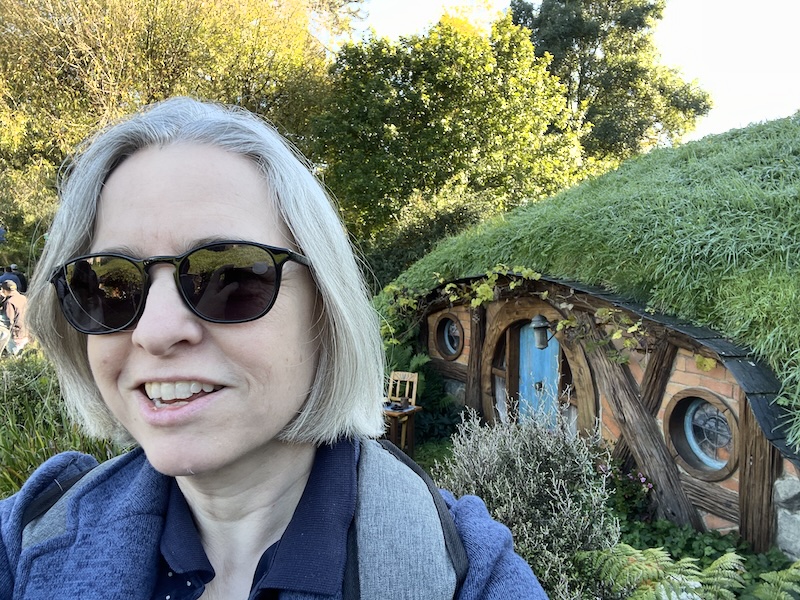 A selfie of me in sunglasses in front of a hobbit hole with a blue door.