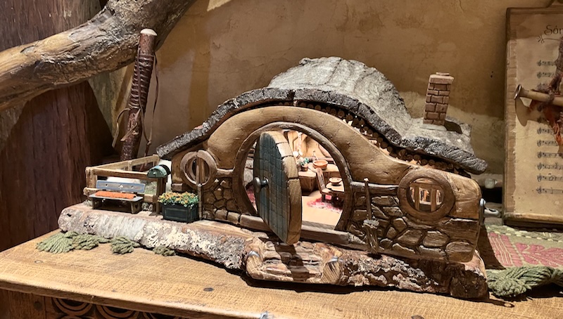 A model hobbit hole showing a lit interior containing small chairs and a table.