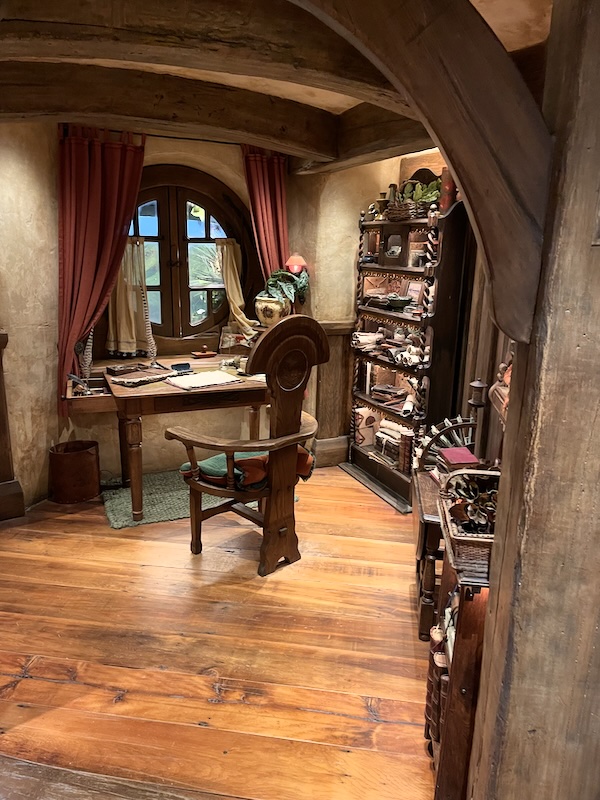 A view into a study with a high-backed chair before a desk. A bookshelf laden with scrolls to one side.