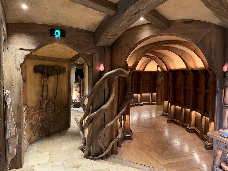 A view of two corridors with arched ceilings. One has hanging brooms. The post between them has curved branches decorating it.