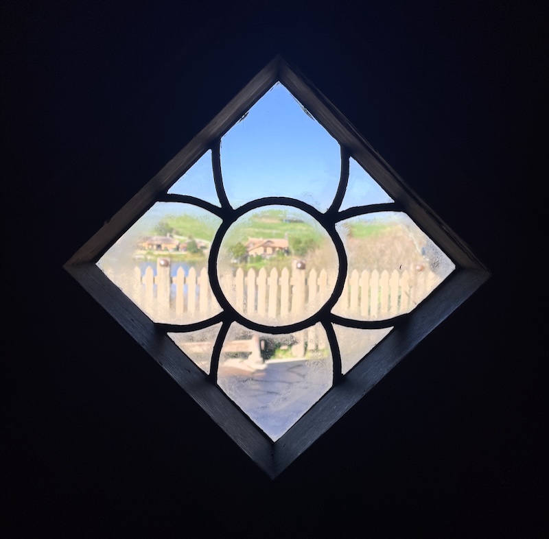 A view through a diamond window showing a wooden fence and the Green Dragon beyond.