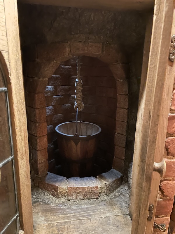 A view into a small room with an brick arch behind which a bucket on a rope hangs over a hole.