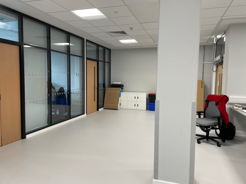 A view of a pillar. A desk and chair are visible to the right and windows and doors to offices on the left.