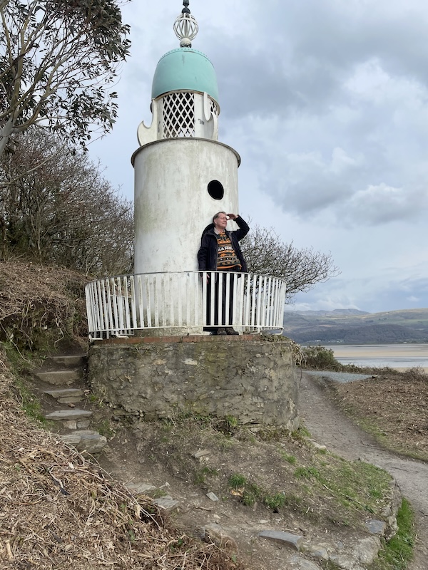 B. stands at the railing of a small lighthouse looking out over the water.