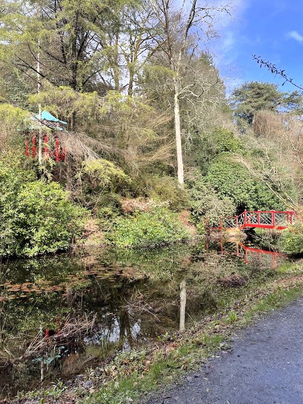 A lake with a red Chinese-style bridge. A red pagoda is visible on the raised bank at the far side of the lake.